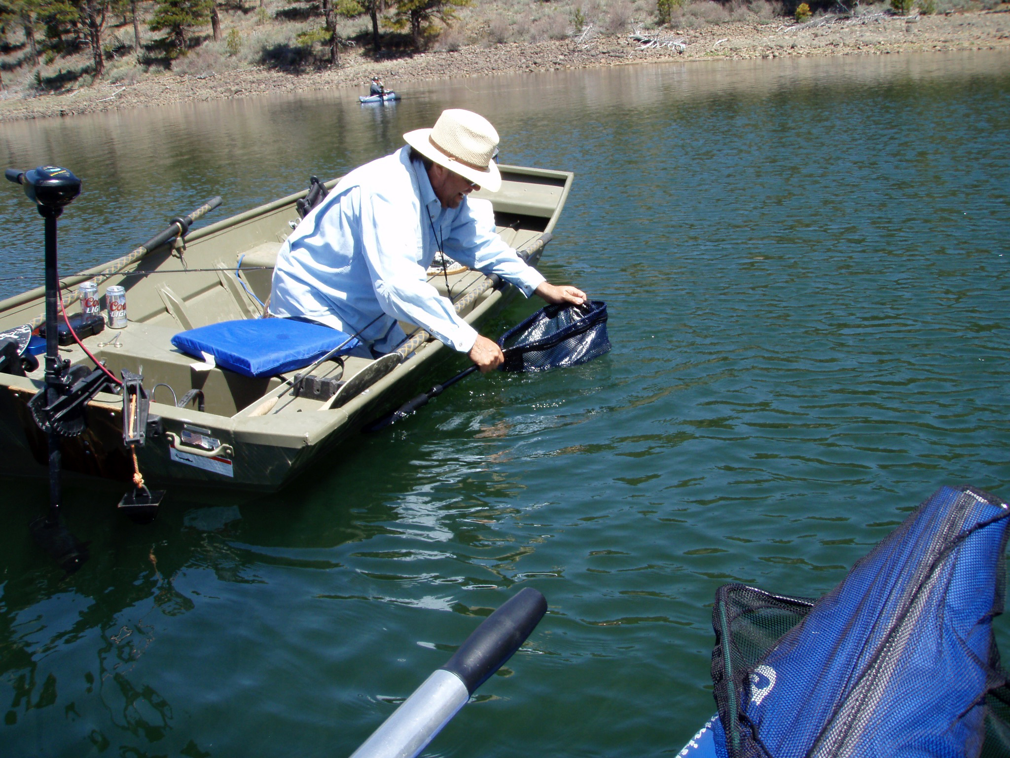 A man smiling and holding a rainbow trout while fishing from a boat on Round Valley Reservoir